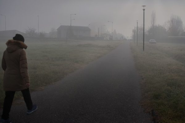 Osoba u toplom kaputu šeta stazom kroz maglovito predgrađe

