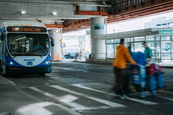 Plavi autobus na putničkoj stanici pored zamagljenih osoba sa prtljagom